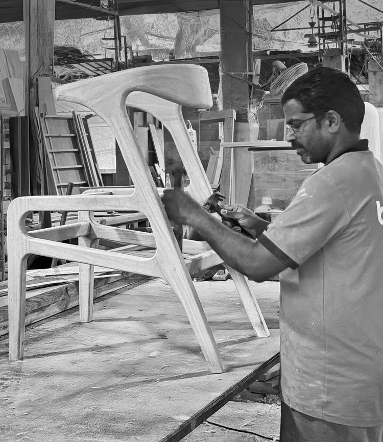 A maker shaping a wooden chair at the factory